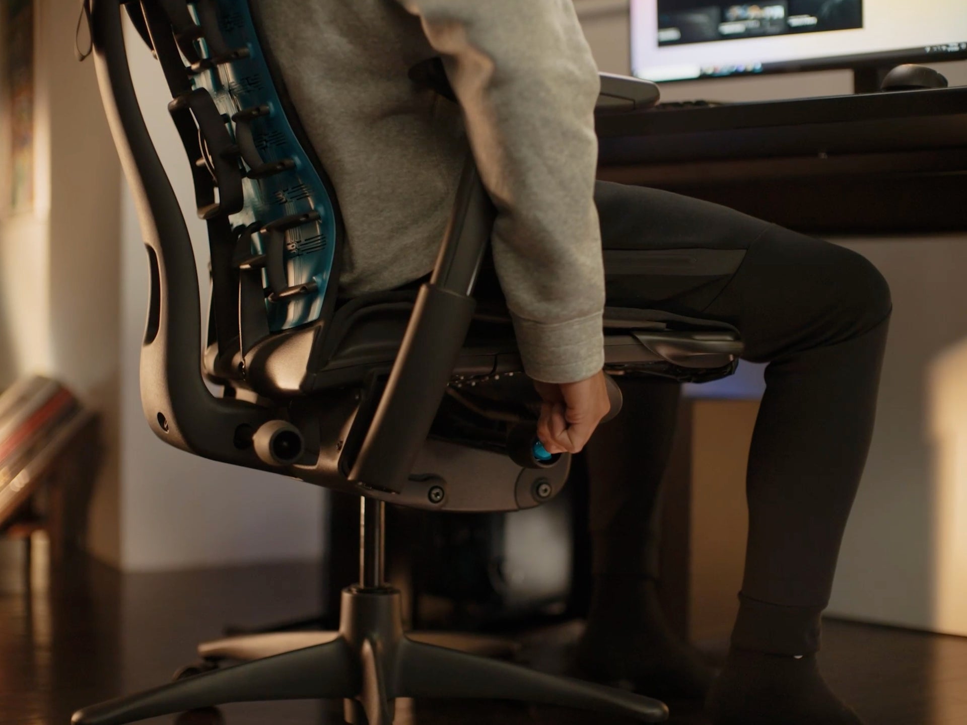 사람이 시트 높이 장치를 조정하는 Embody Gaming Chair의 측면 클로즈업 이미지.