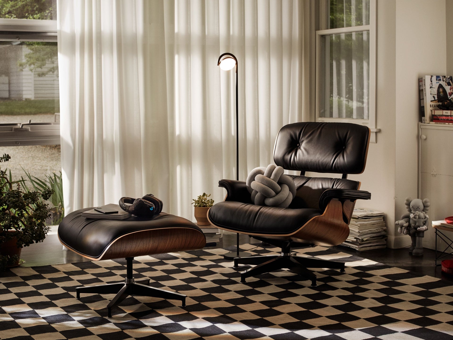 검은 가죽의 Eames Lounge Chair가 체크무늬의 깔개 위에 있습니다.